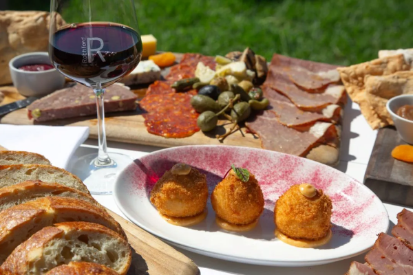 Glass of Rochford red wine beside a charcuterie board and crumbed croquettes at Rochford Wines, Yarra Valley